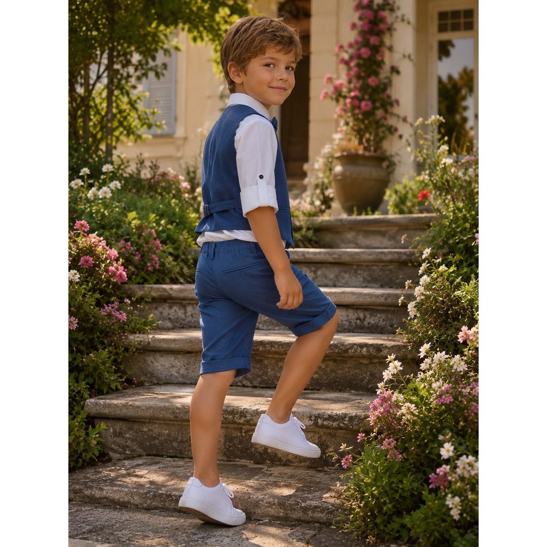 Bambino con gilet e pantaloncino blu e camicia bianca, che sale una scala di pietra fra i fiori
